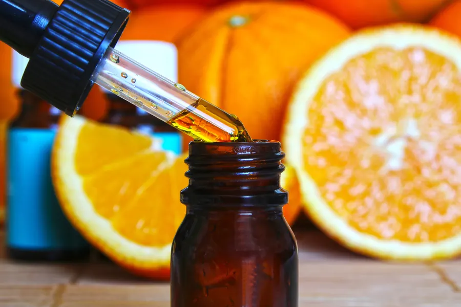 Gotero con aceite esencial sobre un frasco ámbar, con naranjas